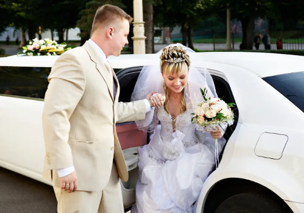 a groom in a suit helping a bridal get out of a car