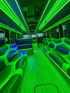 50 passenger party bus interior glowing green with LED light bars, lounge seating, and flat-screen TVs