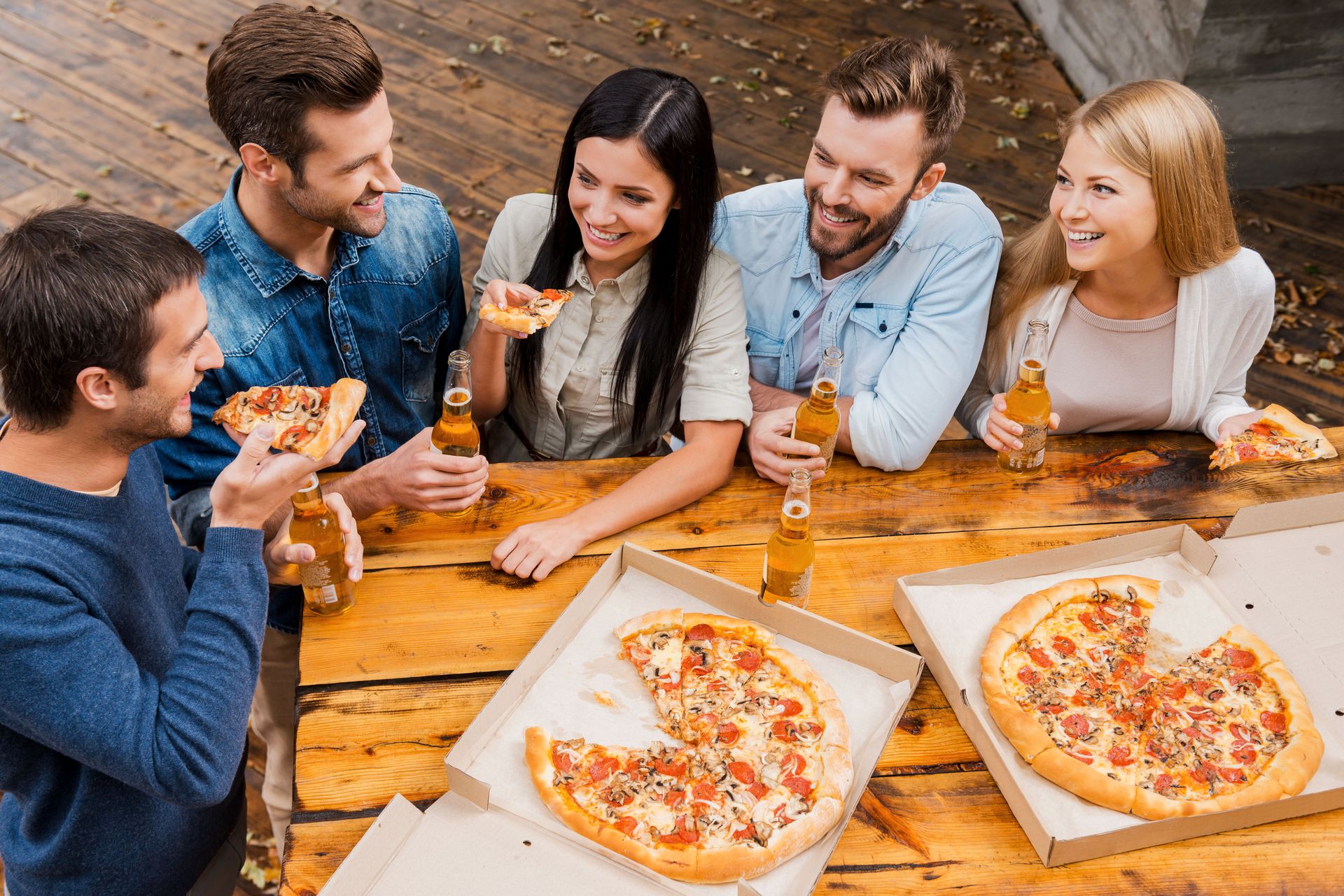Friends eating pizza and drinking beer at an outdoor wooden table