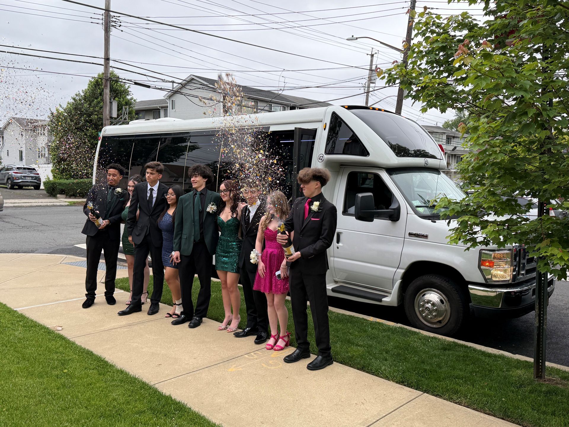 Prom group in formalwear setting off confetti cannons beside a white party bus