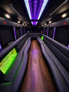 28 passenger party bus interior with purple LED ceiling panel, hardwood floor, and wrap-around leather seating