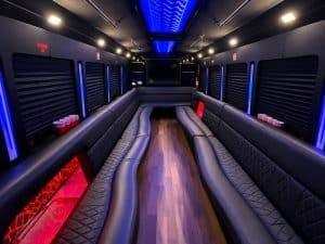 Black 28 passenger party bus interior with quilted leather seating, flat-screen TV, and lit bar