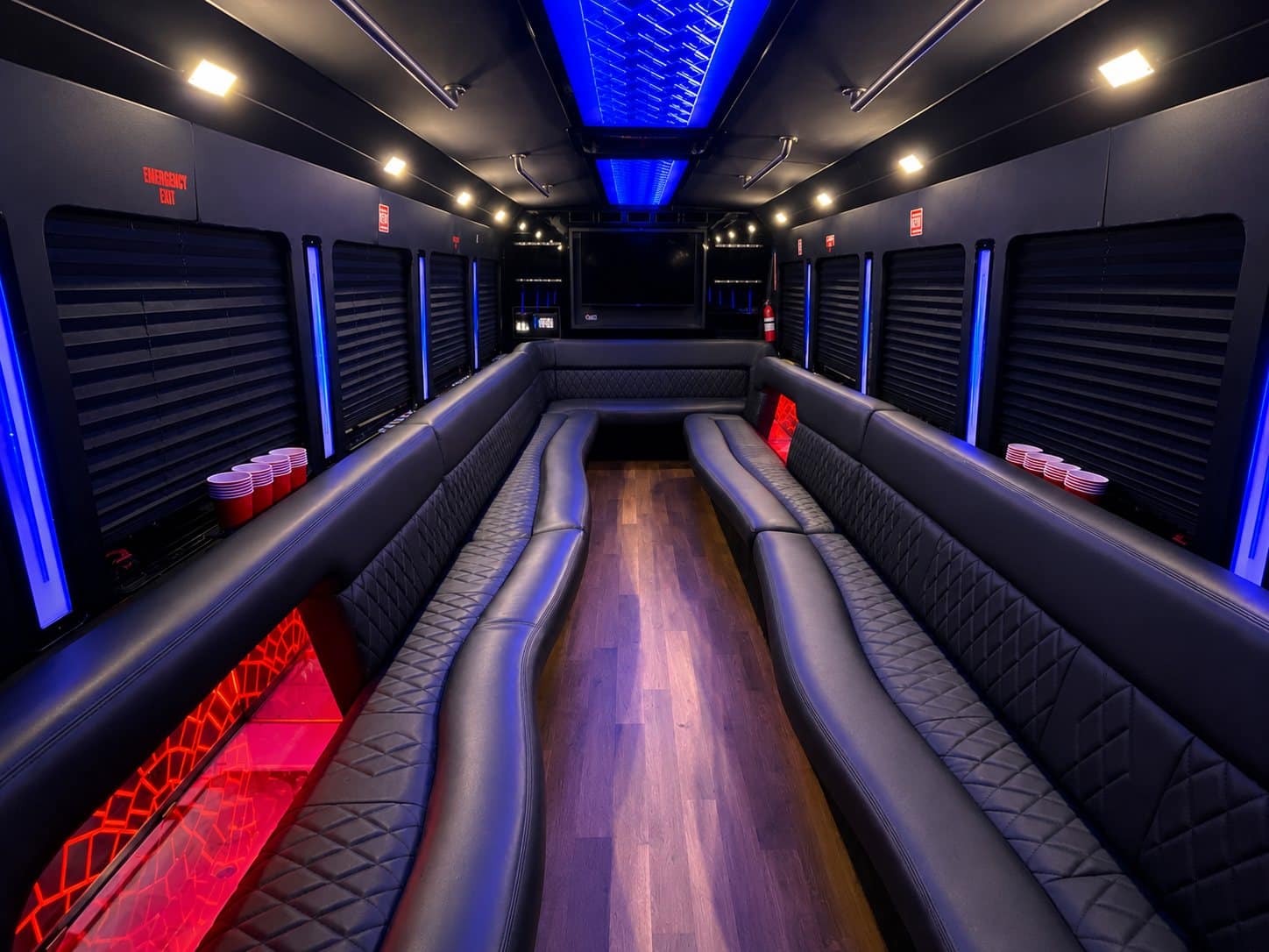 Black 28 passenger party bus interior with quilted leather seating, flat-screen TV, and lit bar