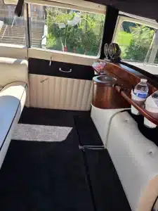 Rear passenger compartment of the 1953 Rolls-Royce classic wedding car, with a burl wood bar, cup holders and cream leather seating